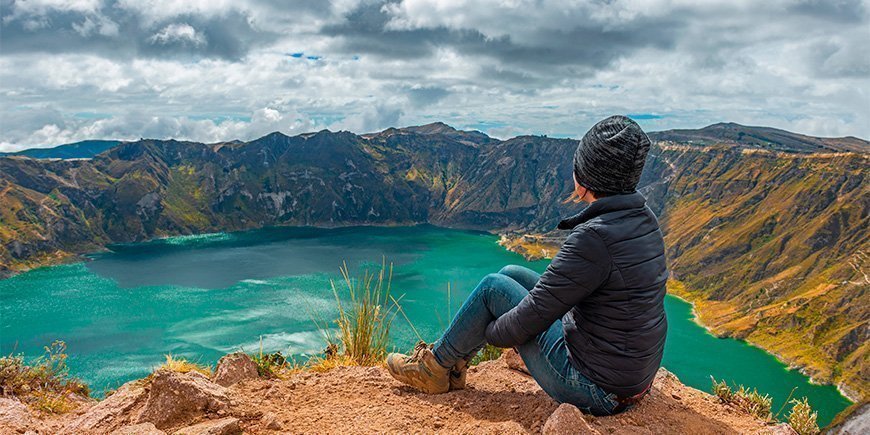 Vrouw zittend aan de rand van het kratermeer Quilotoa in Ecuador.