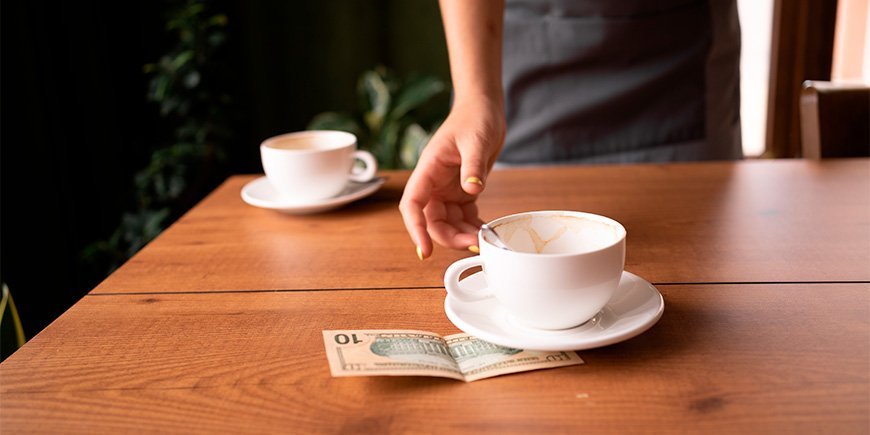 Ober neemt een beker en fooi aan van een tafel in een café