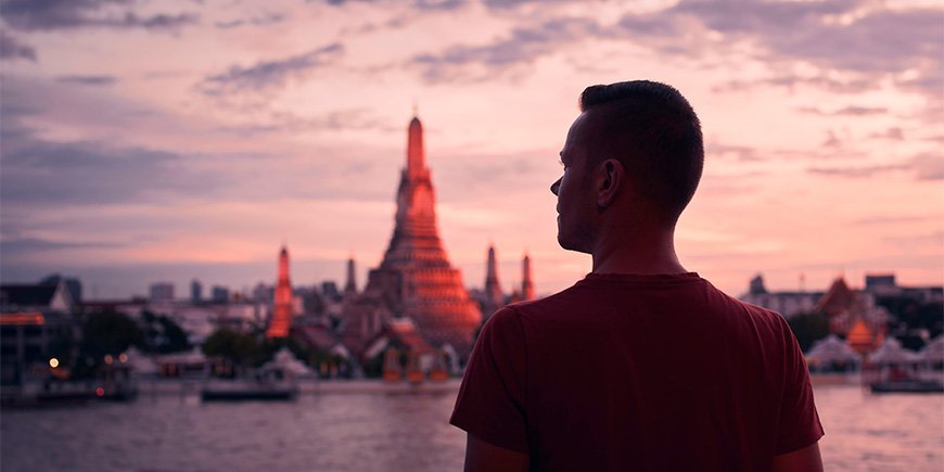 Man staat voor Wat Arun in Thailand bij zonsondergang