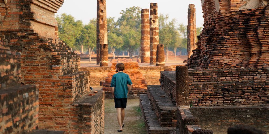 Man loopt bij zonsopgang langs de ruïnes in Sukhothai