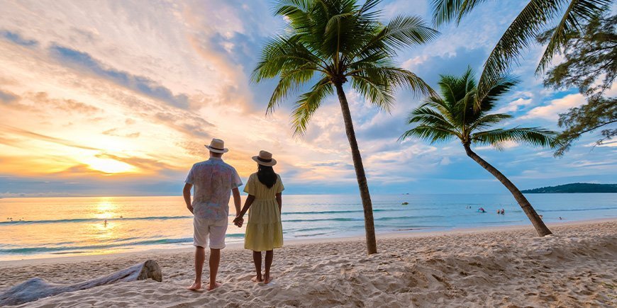 Koppel houdt elkaars hand vast en kijkt naar de zonsondergang op het strand van Phuket